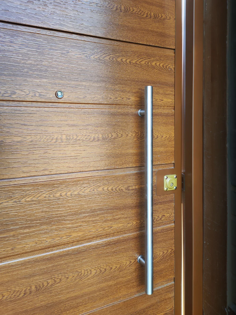 Detalle manillon largo acero en puerta madera instalada en residencia.