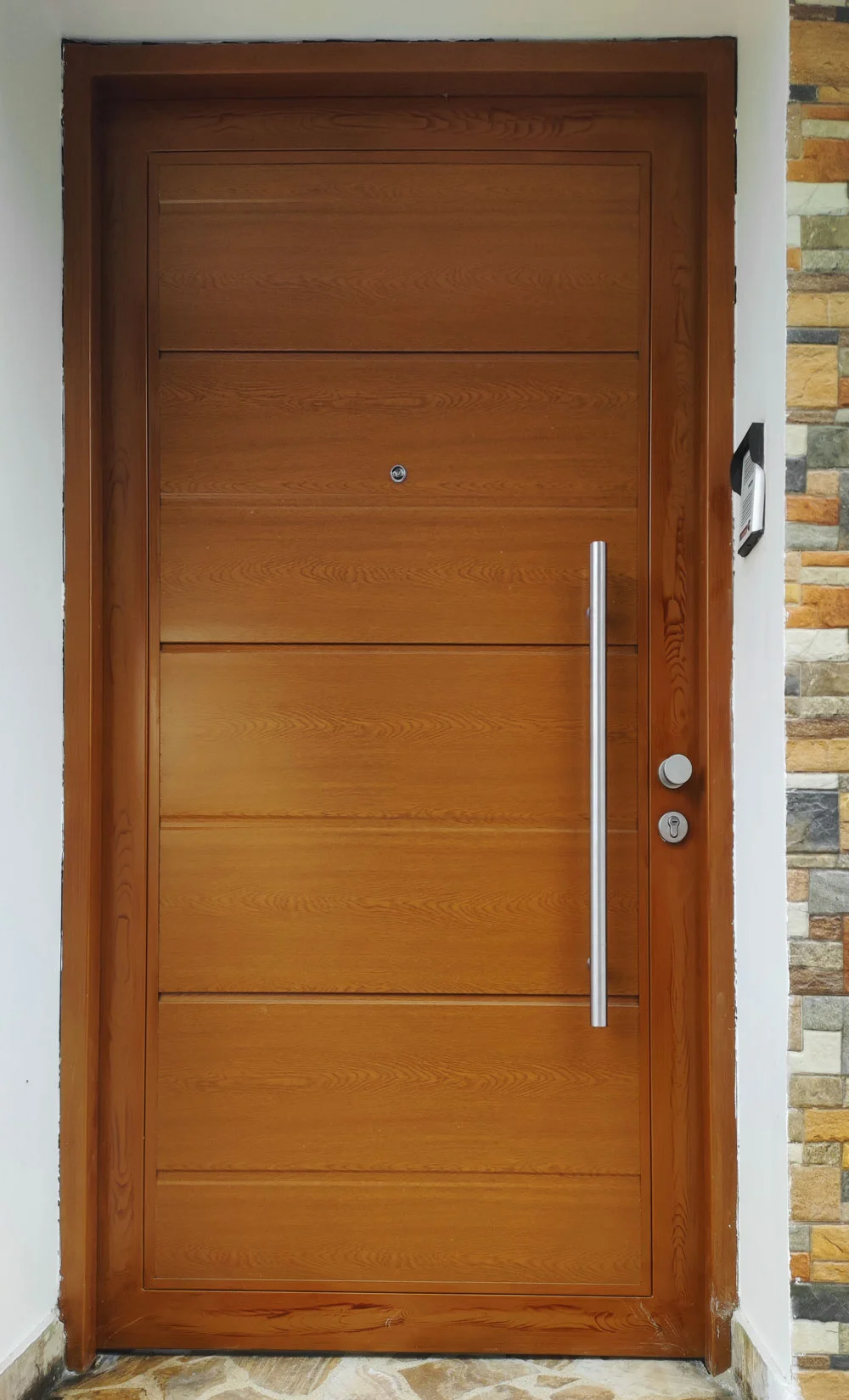 Puerta ingreso madera clara con manillon acero instalada en residencia.